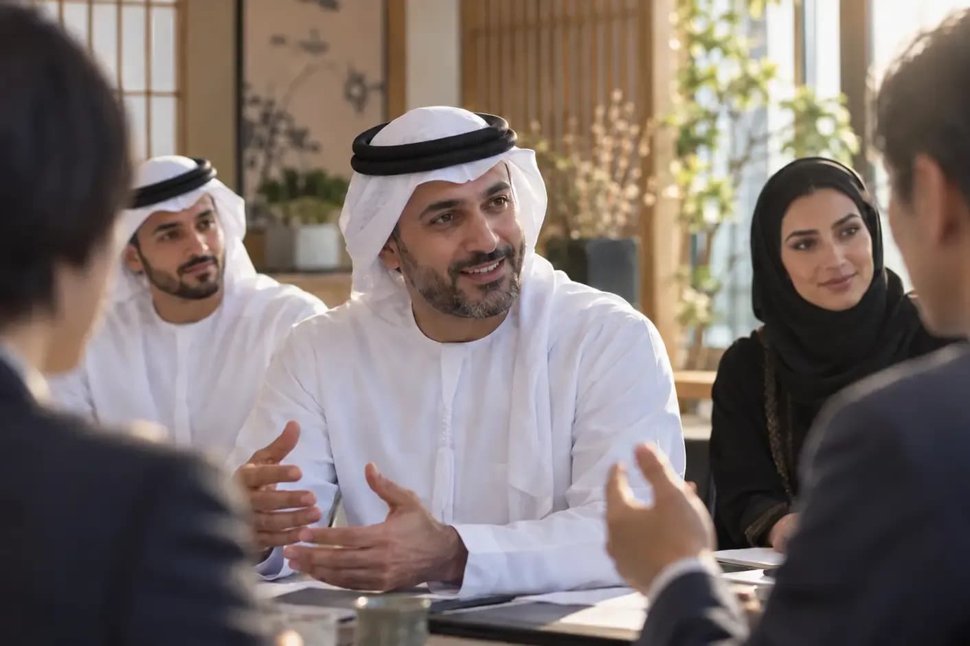 Emirati delegate speaking at a boardroom table with international colleagues during a delegation meeting
